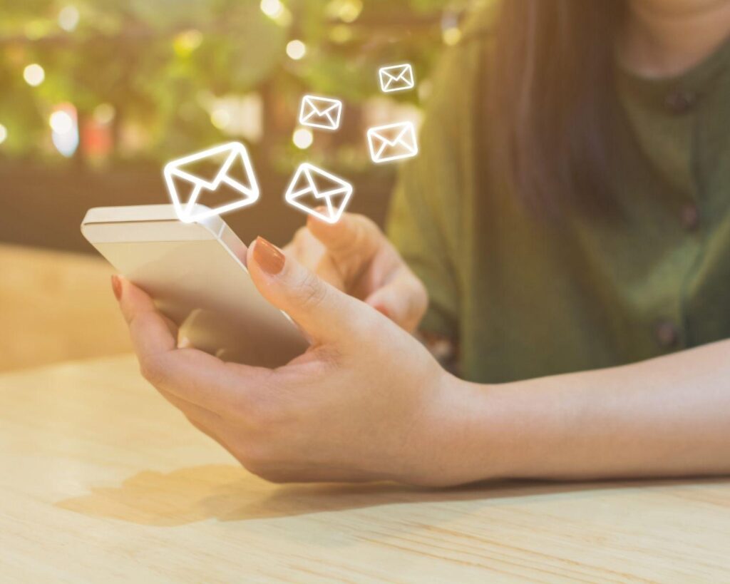 A woman is using a cell phone with email icons coming out of it to increase email open rates.