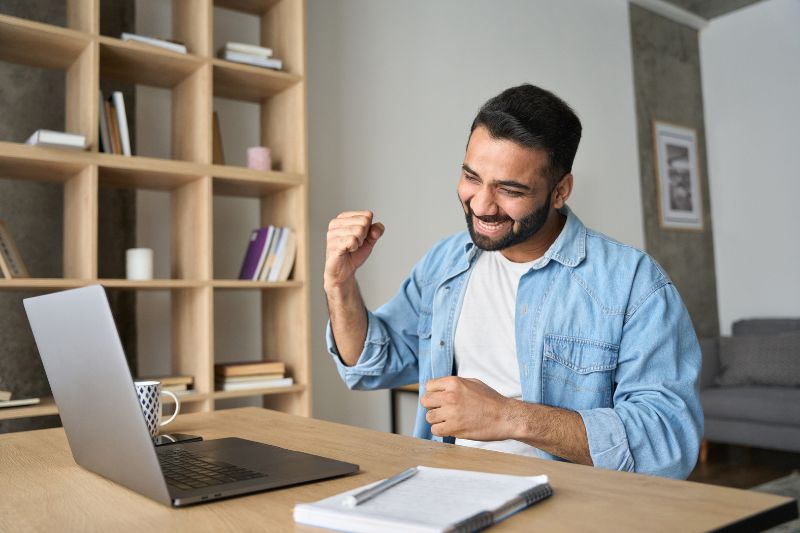 Man celebrating with a fist pump while viewing his laptop screen, likely positive results from email marketing statistics