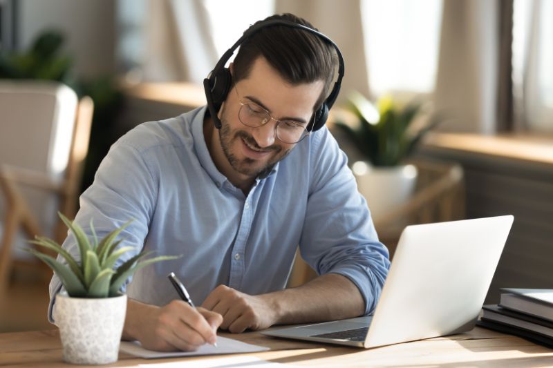 A man taking notes with a pen and a laptop engaged in effective B2B email marketing.