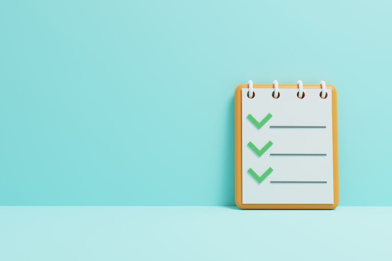 A spiral-bound notepad with three green check marks beside three blank lines against a light blue background, symbolizing the essentials of effective B2B email marketing.