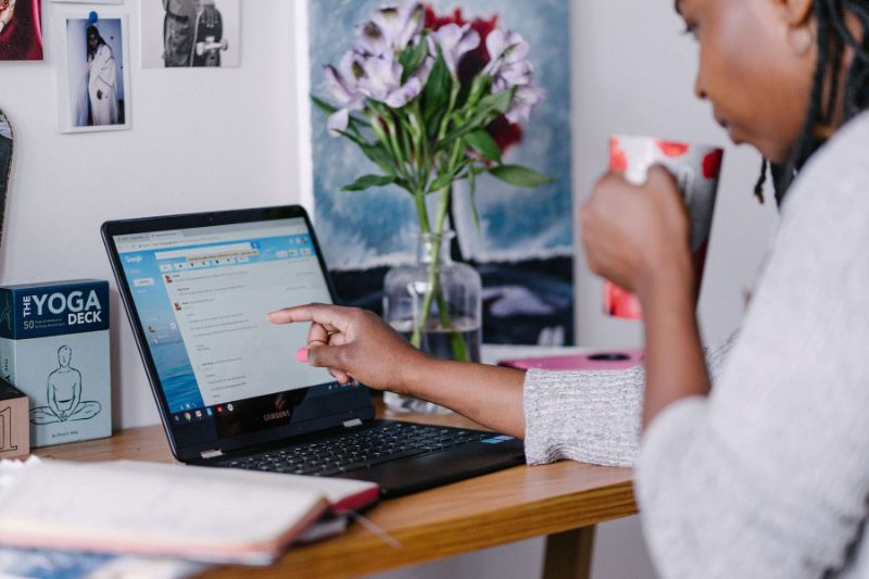 Woman enjoying tea while reviewing email on a laptop and gesturing at the screen