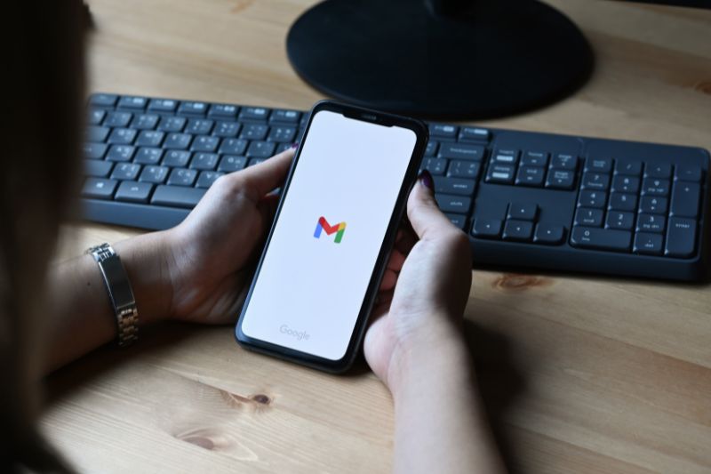 Hand holding a phone displaying the Gmail logo on the screen