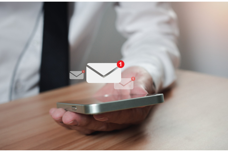 A hand holding a smartphone with incoming emails