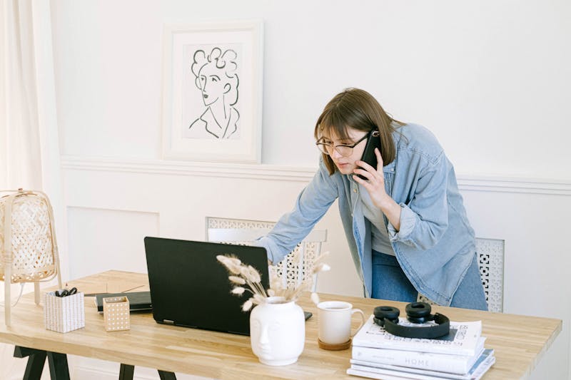 Woman multitasking: having a phone call while working on a laptop, facing the challenge of managing multiple SPF records for a domain.