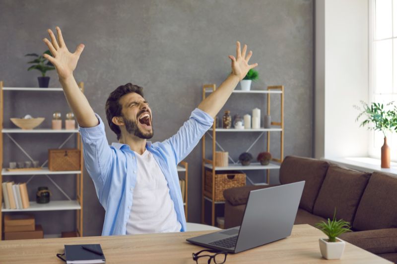 Homem comemorando o sucesso enquanto trabalha em um laptop, possivelmente após resolver o problema de vários registros SPF para um domínio.