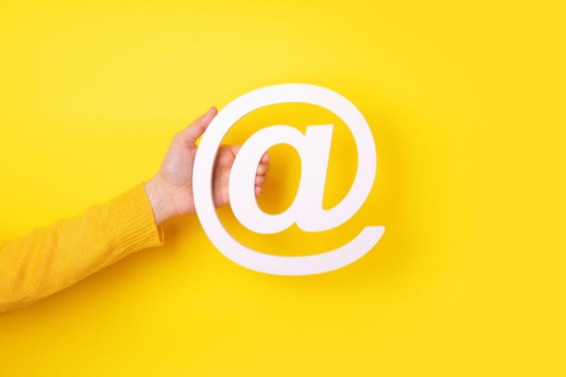Yellow image with a hand holding the "@" symbol, related to email security (SPF and MX).