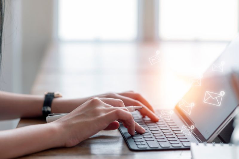 Hand typing on a laptop keyboard, composing an email message