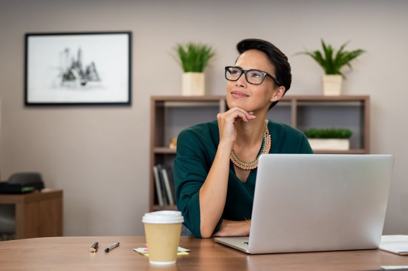 Mulher olhando para cima com um sorriso enquanto usa um laptop