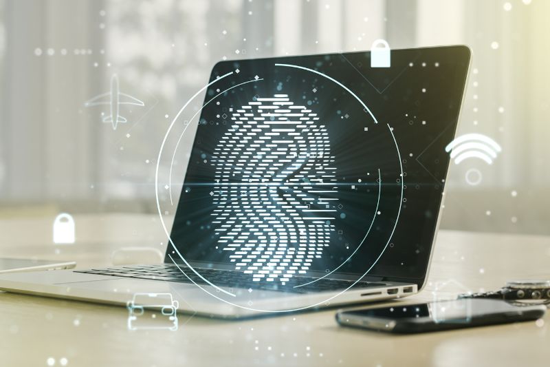 Laptop exibindo um símbolo de cadeado digital na tela, cercado por outros dispositivos e ícones relacionados à escrita de um e-mail frio, sobre uma mesa de madeira.