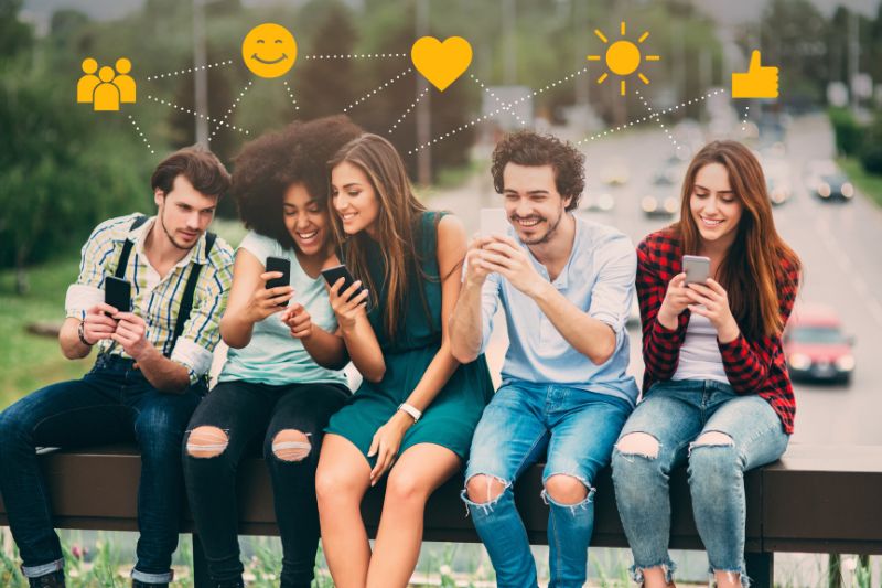 Grupo de cinco jovens adultos sentados juntos, compartilhando conteúdo e sorrindo para seus smartphones enquanto discutem estratégias de e-mail frio.