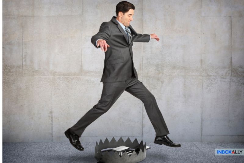 A man in a suit, embodying the precision of spam trap detection, attempts to leap over a bear trap on a concrete floor.