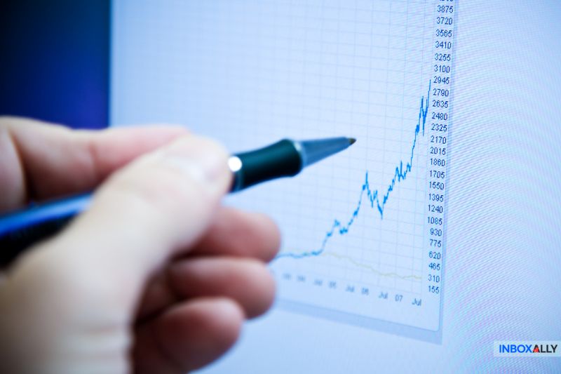 A hand holding a pen points at an upward-trending graph on the screen, reflecting progress akin to overcoming obstacles like Yahoo blocking my emails.