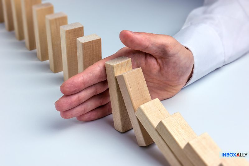 A hand stopping falling dominoes, symbolizing Mailchimp emails going to spam and the need for email authentication and deliverability fixes