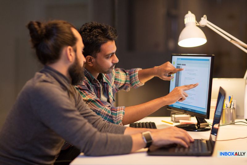 Two people collaborating at a desk, pointing at a computer screen displaying text under a desk lamp, explore growth hack strategies.