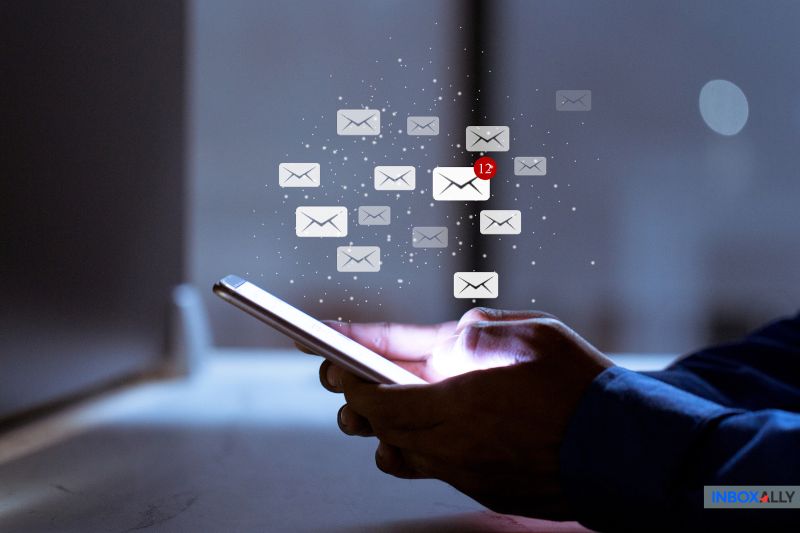 A person holds a smartphone with multiple email icons floating above it, indicating notifications, including one with the number 12—a testament to their active engagement in email marketing strategies.