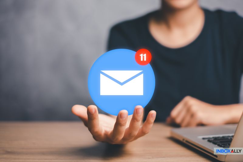 A person holds a digital email icon with the number 11 notification, sitting beside a laptop, contemplating their email marketing strategy.