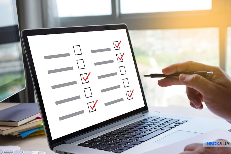 A person using a laptop with a checklist on the screen, holding a pen. Several boxes are checked with red marks, likely setting the email frequency for marketing emails to optimize their reach.