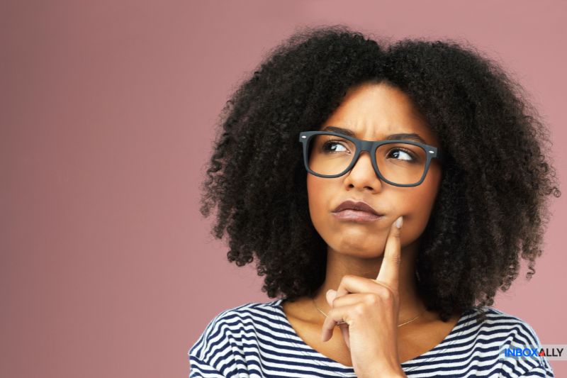 The woman appears deep in thought about email marketing strategies, her finger resting on her chin against a pink background.