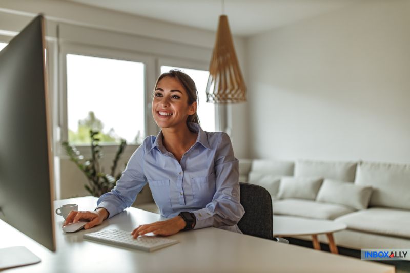 A smiling woman works at her computer in a modern, bright living room, perhaps exploring a guide on navigating Gmail sending limits.