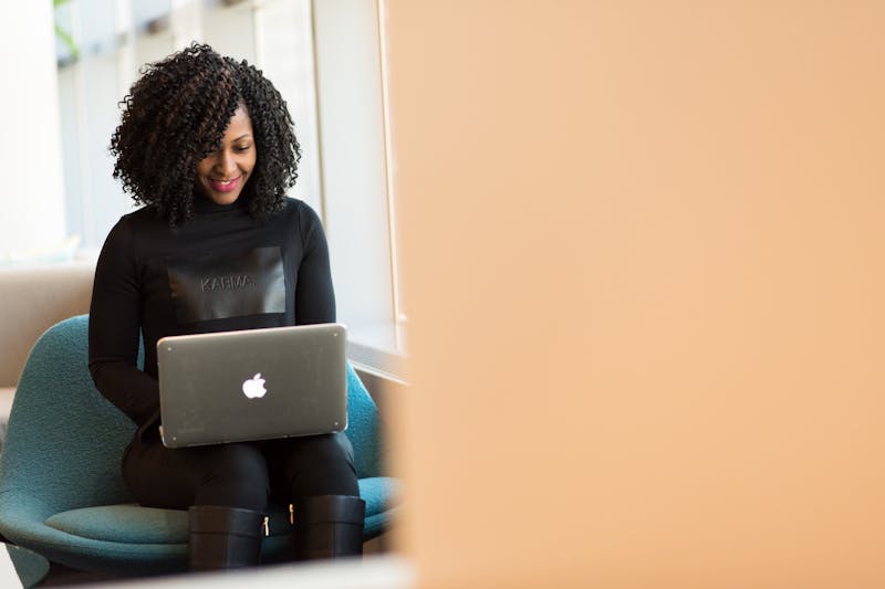 Uma pessoa de cabelos cacheados sentada em uma cadeira, usando um laptop para gerenciar sua caixa de entrada lotada, refletindo sobre a psicologia da reputação do remetente para criar confiança na comunicação.
