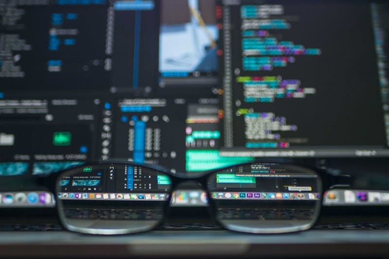 Close-up de óculos apoiados em um teclado de laptop, com código de computador exibido na tela ao fundo, refletindo a psicologia da reputação do remetente.