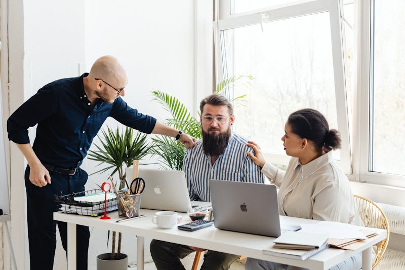 Três colegas de trabalho estão reunidos em torno de uma mesa com laptops em um escritório bem iluminado. Uma pessoa fica apontando enquanto as outras duas se sentam, concentradas em como criar confiança. À medida que se envolvem em uma discussão sobre a caixa de entrada lotada