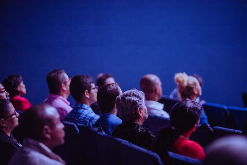 Membros da plateia sentados em um teatro pouco iluminado, cativados pela apresentação, como se estivessem criando confiança com os atores no palco.