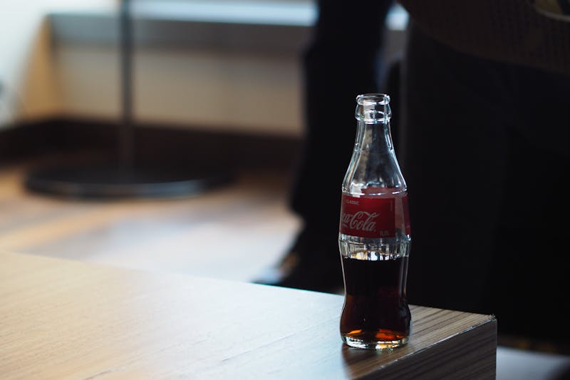 Uma garrafa de Coca-Cola, um símbolo de confiança, fica casualmente na borda de uma mesa de madeira, demonstrando a construção de confiança com seu público.