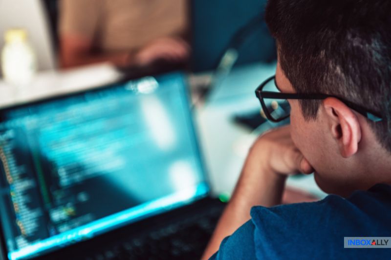 A person wearing glasses intently examines code on a laptop screen, meticulously ensuring they avoid error by double-checking for any "550 5.1.1 User Unknown" error code issues.