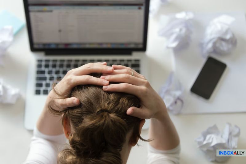 A frustrated individual sits with hands on head, staring at a laptop. The desk is cluttered with crumpled papers and a buzzing smartphone, trying to decipher how to avoid an 'Error Code' that's disrupting their workflow.