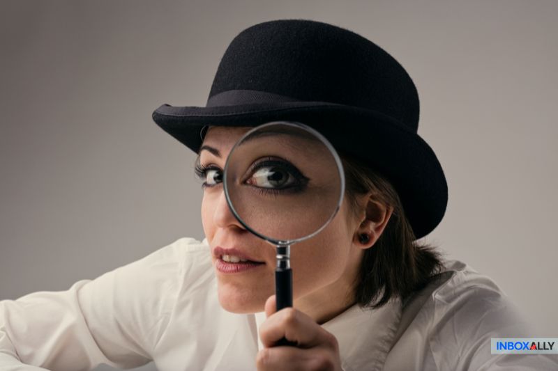 A person wearing a bowler hat holds a magnifying glass close to one eye, creating an enlarged effect. They're dressed in a white shirt and looking directly at the camera, embodying how marketers strive for AI email personalization while retaining a genuine human feel.