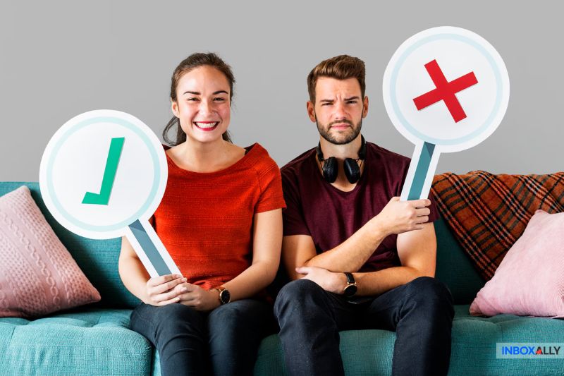 Two people sitting on a couch engage in a lighthearted debate. The woman, confident in her stance, holds up a checkmark sign and smiles. The man, pondering the issue of an effective hosted email spam filter, holds an X sign with a doubtful expression.