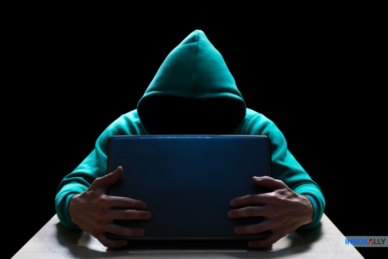 A person in a green hoodie sits at a table, intently scrutinizing their laptop. The face is obscured, and the background is dark—a perfect setting to ensure they do not get tricked by a spam order confirmation email.