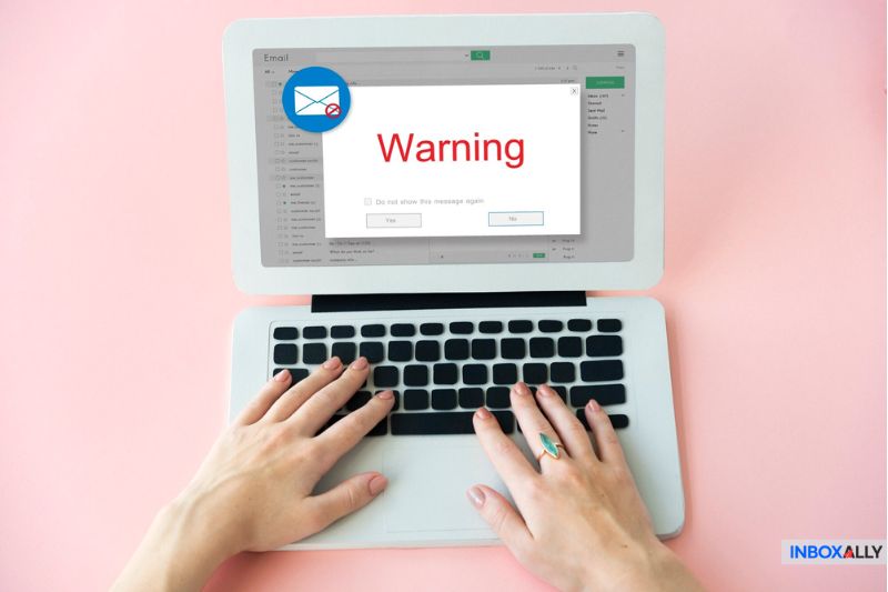 Hands typing on a laptop with a warning about email spam on the screen, set against a pink background.