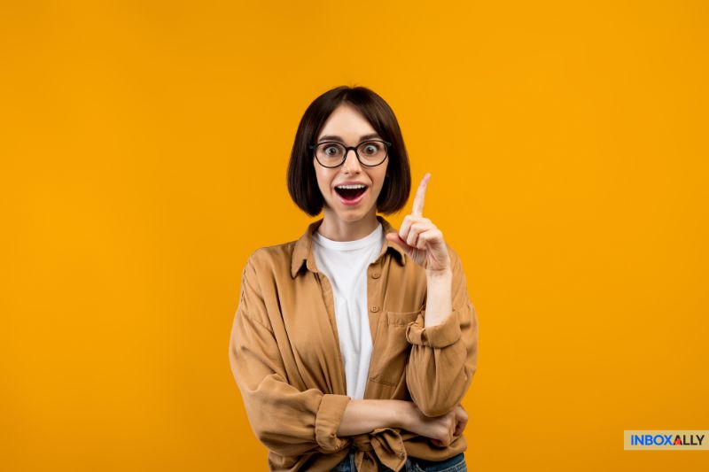 A person with short hair and glasses, in a brown shirt over a white t-shirt, raises one finger in excitement against a solid yellow background, as if they just realized the email wasn’t spam but an actual order confirmation.