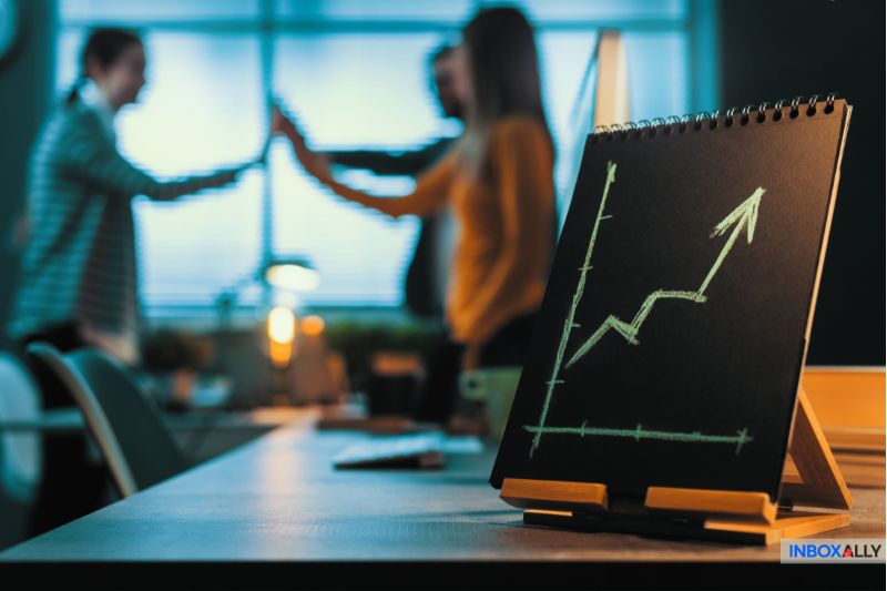 A small easel displays a green upward-pointing graph, suggesting innovative growth worth trying. In the background, three people celebrate with high-fives in an office setting, possibly discussing promising strategies or AWeber alternatives for 2025.