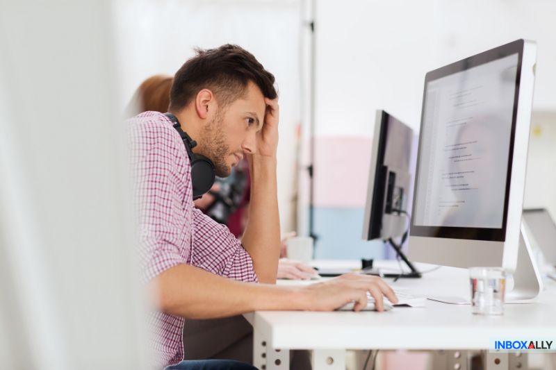 Um homem está sentado em uma mesa, olhando para a tela do computador com uma expressão preocupada, apoiando a cabeça em uma das mãos - preocupado com um erro de SPF que afeta a capacidade de entrega de seu e-mail.