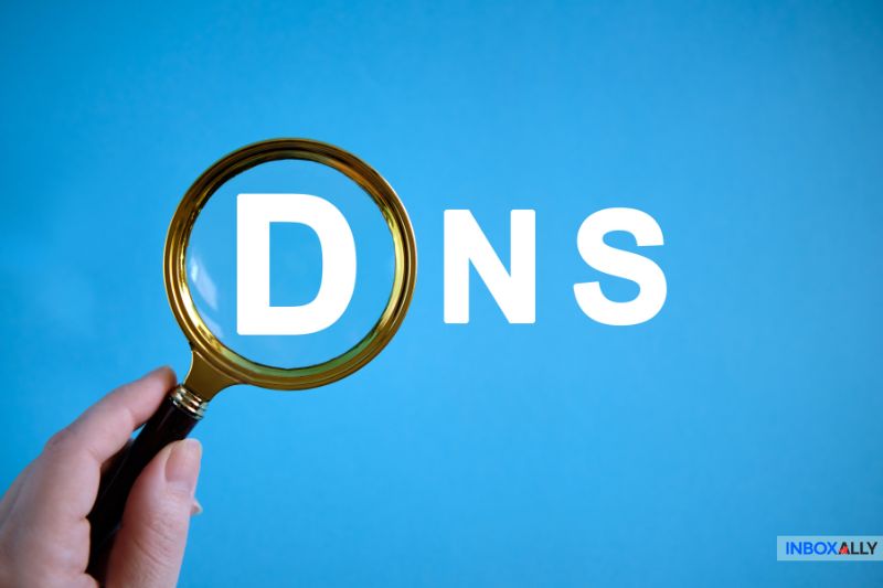 A hand holds a magnifying glass over the letter "D" in the word "DNS" against a blue background, suggesting investigation of issues like email delivery problems or the 550 5.7.0 error.