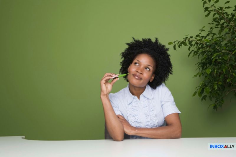 A woman sits at a white table against a green background, holding a small plant and looking thoughtfully upward. A leafy plant, the InboxAlly logo, and mention of a disposable email address are visible in the scene.